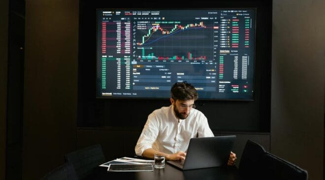 Businessman using laptop in office analyzing stock market charts. Professional finance and investment concept.